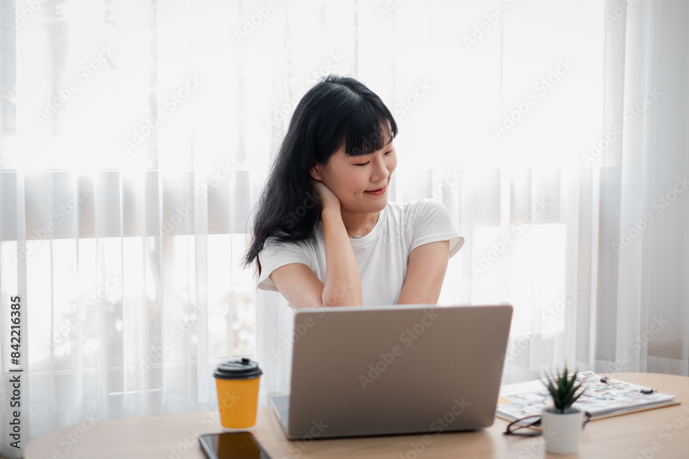 Young woman working on a laptop at a home office desk with coffee and plant, bright natural light through sheer curtains. Young woman working on a laptop at a home office desk with coffee and plant, bright natural light through sheer curtains.