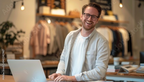 Smiling man with glasses working on laptop in a retail store.