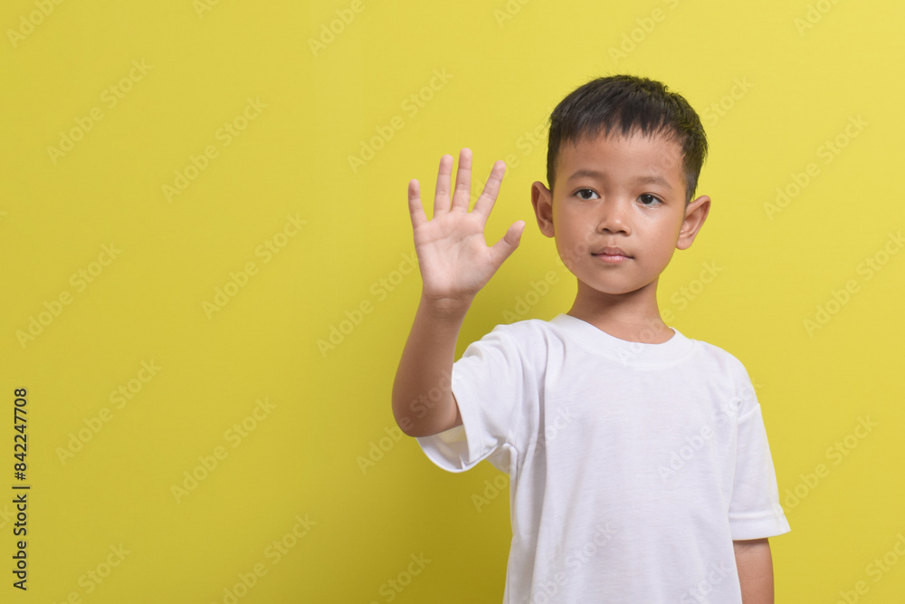Image of Asian child posing raising his hand with five fingers, cute and smiling happily on a yellow background. portrait of an Asian boy. Copy space Image of Asian child posing raising his hand with five fingers, cute and smiling happily on a yellow background. portrait of an Asian boy. Copy space