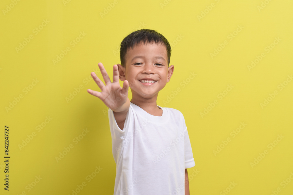 Image of Asian child posing raising his hand with five fingers, cute and smiling happily on a yellow background. portrait of an Asian boy Image of Asian child posing raising his hand with five fingers, cute and smiling happily on a yellow background. portrait of an Asian boy