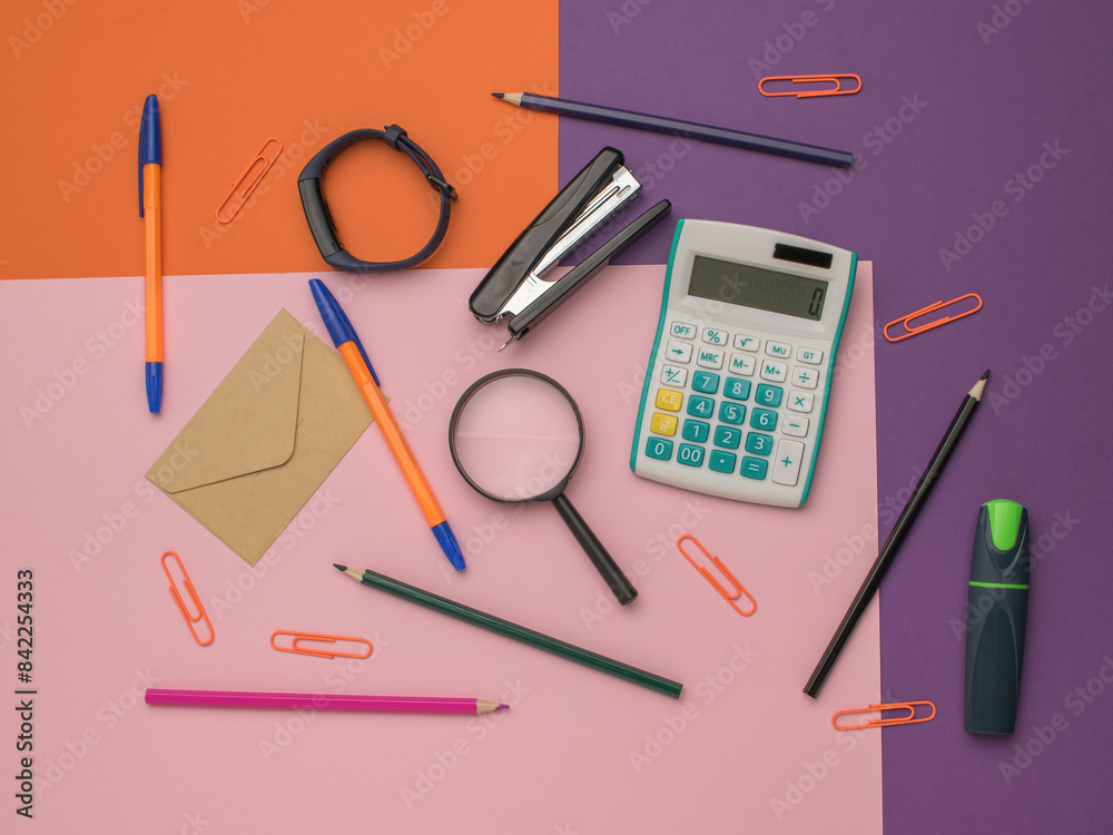 Top View of Office Supplies: Calculator, Pens, Stapler, Magnifying Glass on Colorful Background Top View of Office Supplies: Calculator, Pens, Stapler, Magnifying Glass on Colorful Background