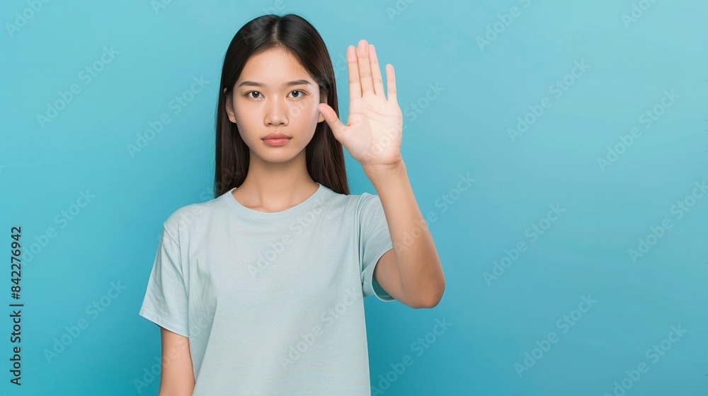 Young asian woman making stop gesture with her hand on blue background. Disagree with something.