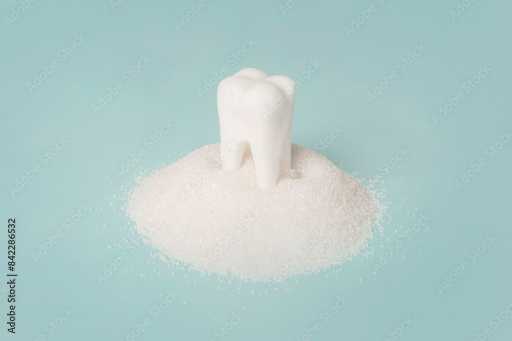 Fototapeta premium Tooth with sugar on blue background. Harm of sugar and sweet for teeth, care. concept, tooth loss