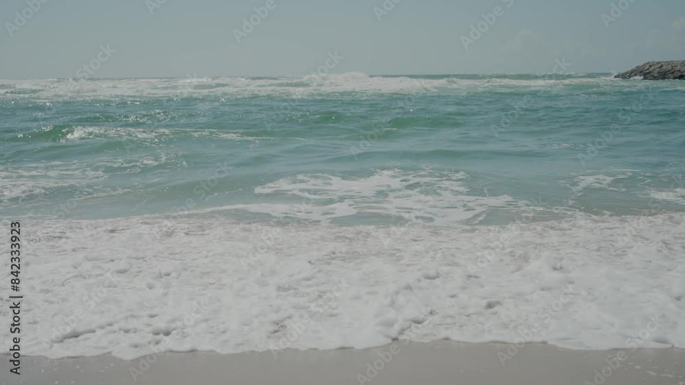 Waves crashing on the sandy beach with clear blue water and a sunny sky Waves crashing on the sandy beach with clear blue water and a sunny sky