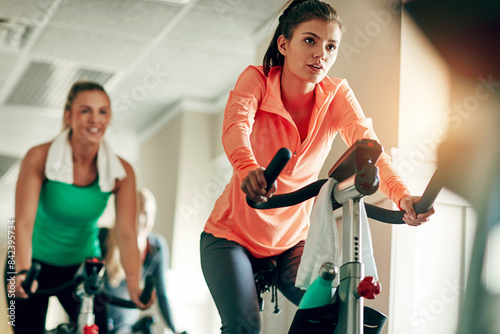 Woman, cycling and workout with spin class at gym for cardio exercise or indoor training together. Active female person or group of cyclists riding on equipment or bicycle for fitness at health club