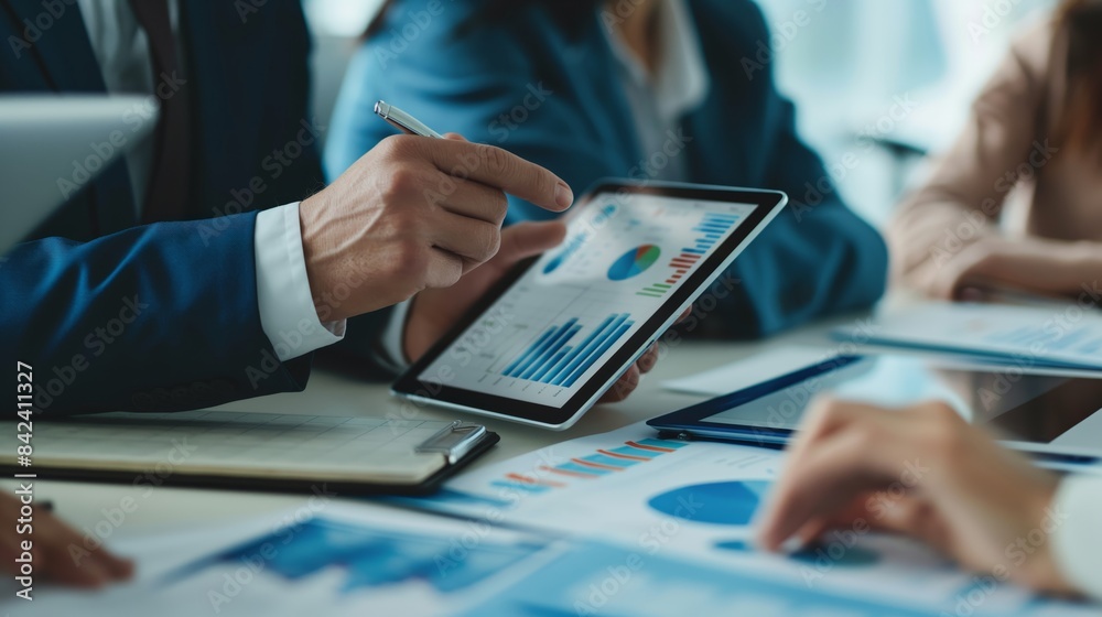 A team of professionals collaborates on financial data analysis using a tablet A team of professionals collaborates on financial data analysis using a tablet