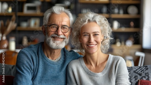 An elderly couple smiles warmly at the camera, showcasing a loving bond in their comfortable living space