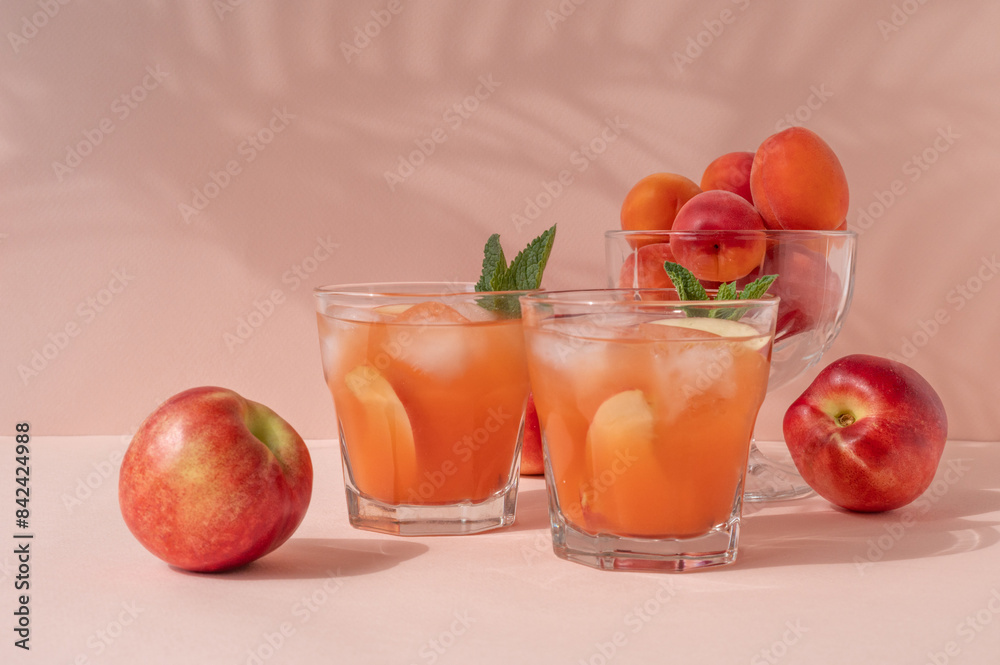 Fresh summer peachy fruit mocktail drinks with ice, sweet peaches and nectarines on pink background with soft shadows Fresh summer peachy fruit mocktail drinks with ice, sweet peaches and nectarines on pink background with soft shadows
