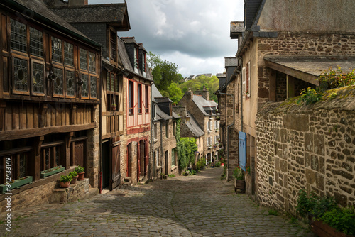 View of the medieval street of the city with half-timbered houses descending to the embankment of the Rance River on a sunny summer day, Dinan, Cotes-d'Armor, Brittany, France