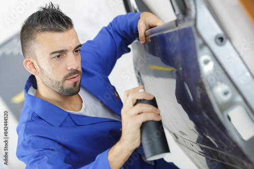 man spraying car door with tinned paint
