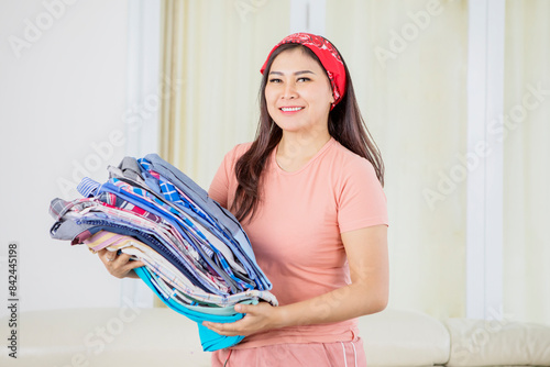 Beautiful Asian woman smiling to camera while holding a pack of clothes in a living room