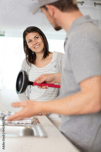 happy woman looking at plumber using plunger in the sink