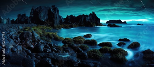 A serene beach at night with blue waves lighting up a lone rock formation under the moonlit sky  providing a perfect copy space image.