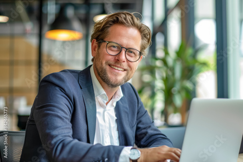 Professional Man with Glasses Working at Laptop, Bright Office Setting