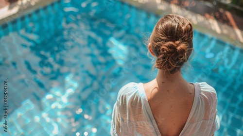 A young woman stands dejectedly by a pool, her sunburnt back covered in a loose shirt, showcasing the disruption sunburn can cause on a trip.