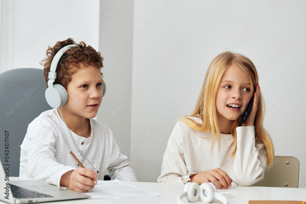 Happy Caucasian boy and girl studying at home with their laptops They are sitting in the living room, wearing headphones and concentrating on their online elearning lessons Technology and connection Happy Caucasian boy and girl studying at home with their laptops They are sitting in the living room, wearing headphones and concentrating on their online elearning lessons Technology and connection