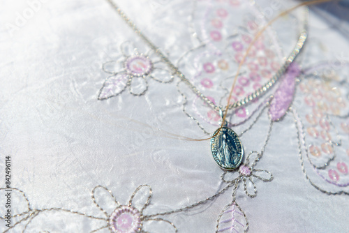 A silver medallion on a chain, placed on a beautiful white fabric embroidered with flowers and butterflies
