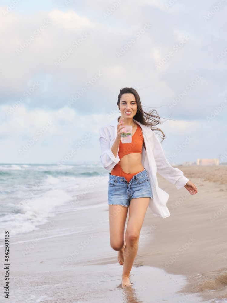 A woman is running on the beach with a cup in her hand A woman is running on the beach with a cup in her hand