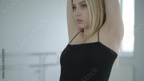 Fit girl in black clothes performing contemporary. Female dancer shows flowing motions, body and hands waves at white room. Modern ballet dance choreography. Young woman is moving smoothly photo