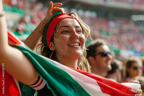A smiling young woman with a headband holding a national flag, showing pride and enthusiasm at a sports event