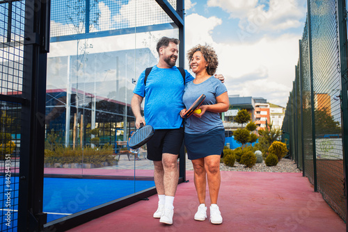 фотографія Smiling mix couple comes to the outdoor court to play padel.