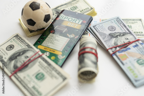 Smartphone with gambling mobile application and soccer ball with money close-up. Sport and betting concept