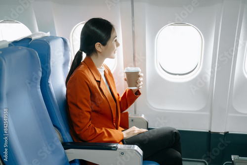 Asian businesswoman or entrepreneur in a formal suit on an airplane sitting in business class using a phone, computer laptop. Travel in style, work