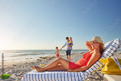 Woman, blue sky and relax on beach chair with family together, adventure and bonding in summer holiday. Happy, mother and sunglasses by ocean, travel and freedom for tropical vacation in Greece © peopleimages.com