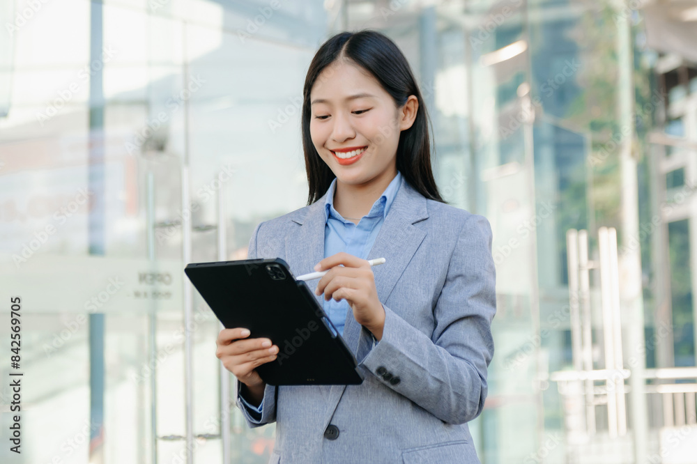 Young Asian business woman leader entrepreneur, professional manager holding digital tablet computer on the street in big city on business center background.. Young Asian business woman leader entrepreneur, professional manager holding digital tablet computer on the street in big city on business center background..