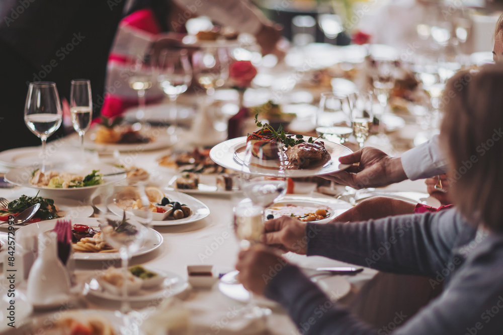 Waiter serving table in the restaurant preparing to receive guests. Waiter carrying plates with meat dish on some festive event. Waiter serving table in the restaurant preparing to receive guests. Waiter carrying plates with meat dish on some festive event.
