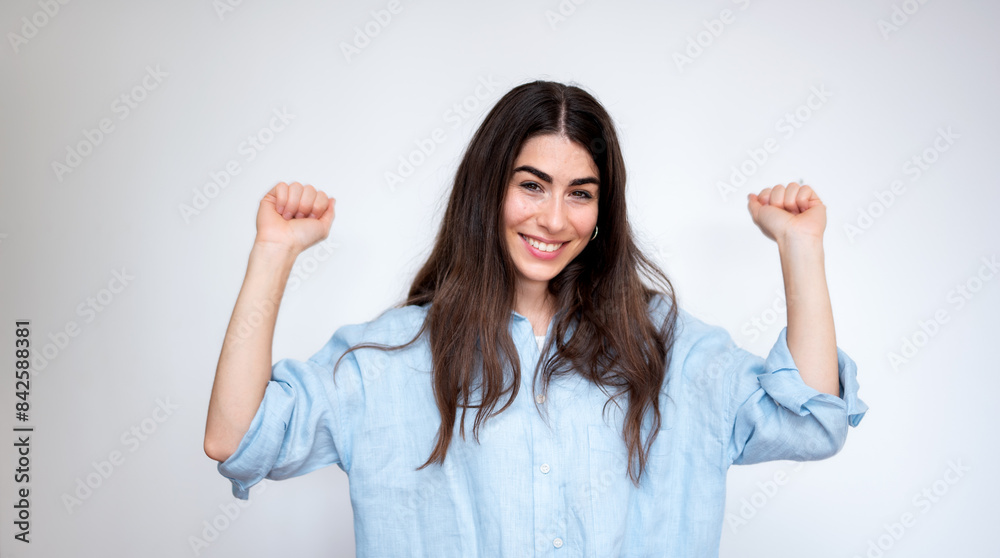 Young woman is celebrating success with arms raised and clenched fists Young woman is celebrating success with arms raised and clenched fists