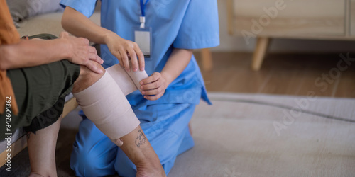 Close up of Asian caregiver bandaging elderly woman's leg at home. Concept of elderly care and wound management