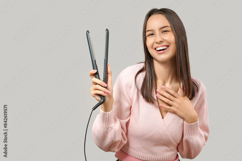 Beautiful young woman with hair straightener on light background Beautiful young woman with hair straightener on light background