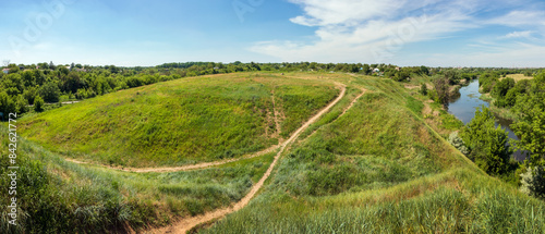 Donets Hillfort is an archaeological site in Kharkiv city, Ukraine. Panoramic view of the hill on the site of an ancient settlement next to the river. Grass-covered hill and walking path photo
