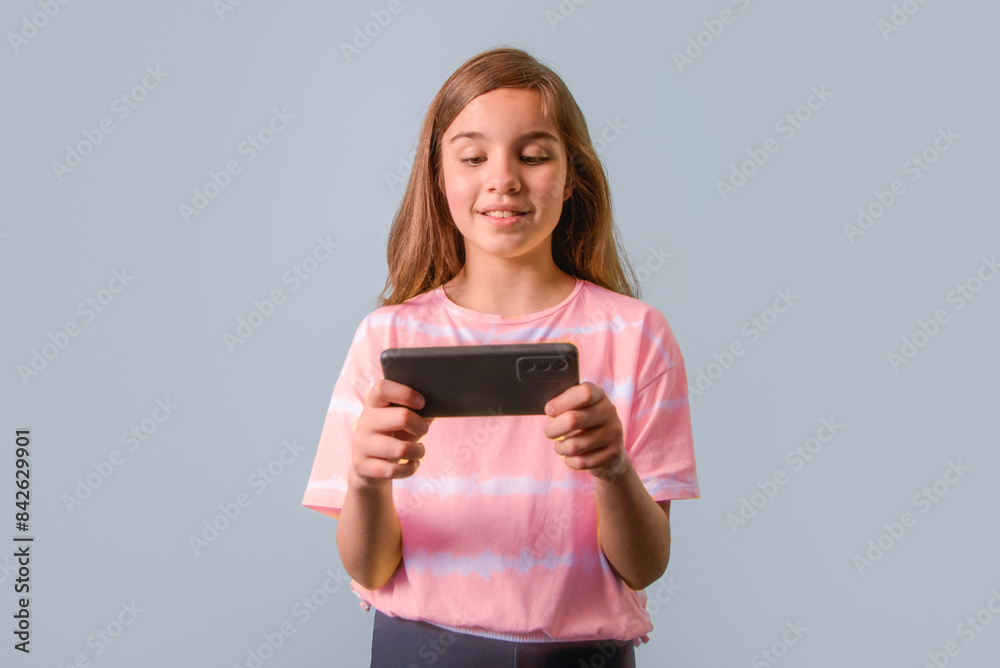 A girl is holding a cell phone and smiling. She is wearing a pink shirt. A girl is holding a cell phone and smiling. She is wearing a pink shirt.