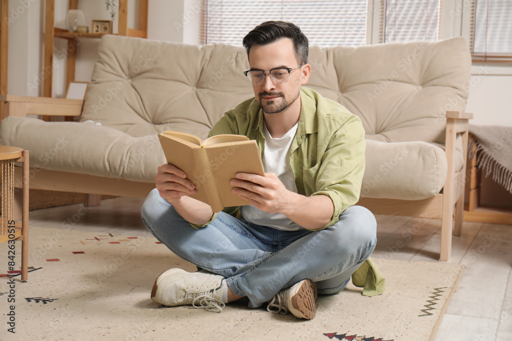 Handsome young man in eyeglasses sitting at home in lotus position and reading book Handsome young man in eyeglasses sitting at home in lotus position and reading book