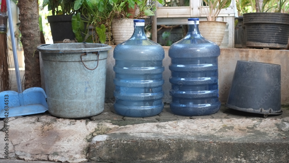 Fototapeta premium Plastic waste items, recycled items, empty water gallons, plastic and paper buckets to save the environment. Green tree background. Environmental saving concept.