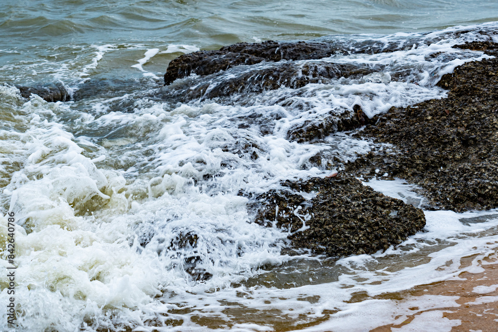 View of white foamy after sea wave splashing the big rocks on golden beach of Pattaya City, Thailand. View of white foamy after sea wave splashing the big rocks on golden beach of Pattaya City, Thailand.
