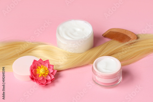 Blonde strand with jars of hair mask  comb and flower on pink background  closeup