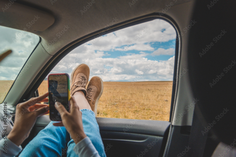 Naklejka premium A person is laying in a car with their feet up and looking at their phone. Huayllay Stone Forest, Peru.