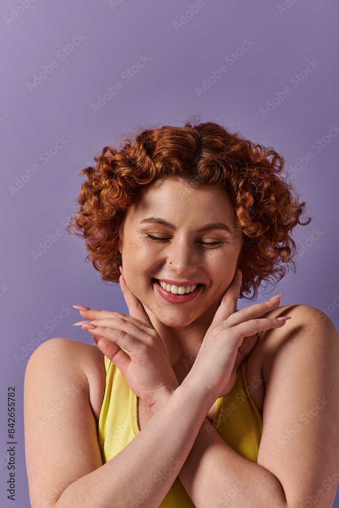 A young, curvy redhead woman in yellow underwear strikes a playful pose, hands on face, against a purple background. A young, curvy redhead woman in yellow underwear strikes a playful pose, hands on face, against a purple background.