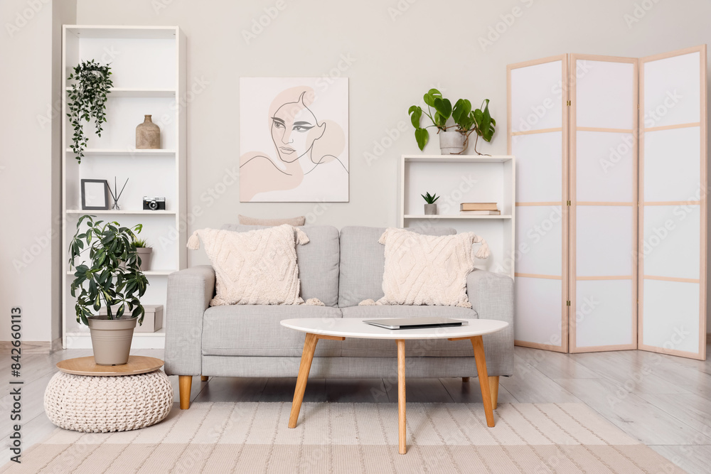 Fototapeta premium Light living room with folding screen, comfortable sofa, coffee table and shelving unit
