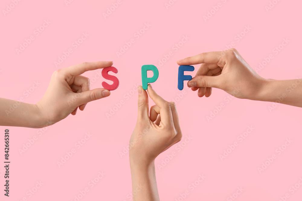 Female hands with letters SPF on pink background Female hands with letters SPF on pink background