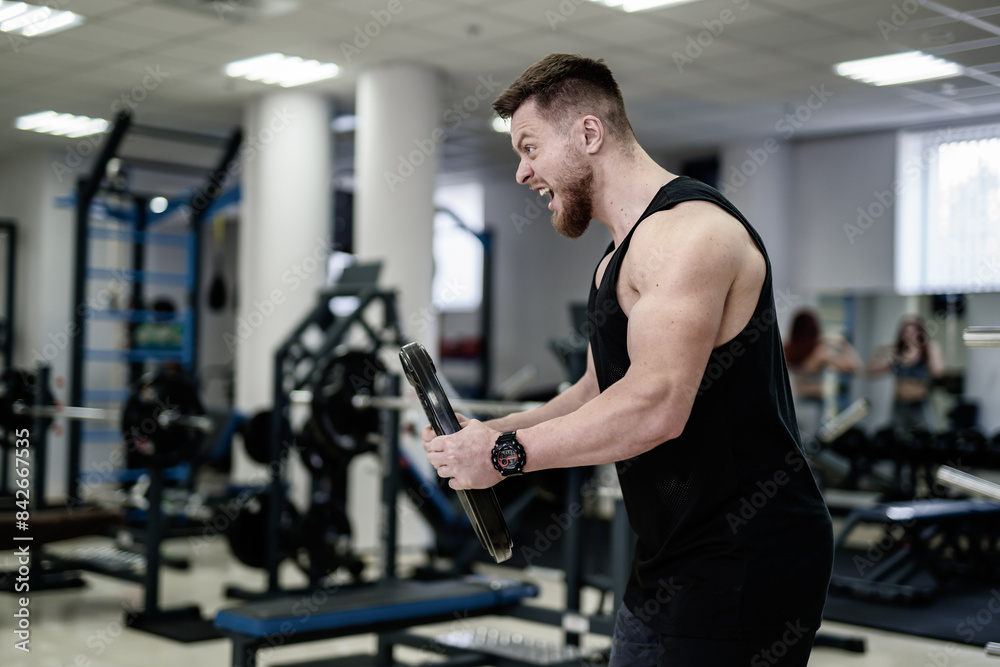 A man in a black tank top is holding a weight in his hand and appears to be angry A man in a black tank top is holding a weight in his hand and appears to be angry