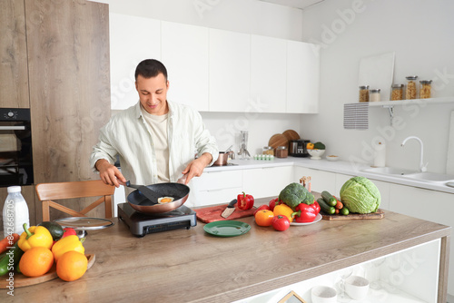Young man frying eggs in ki...