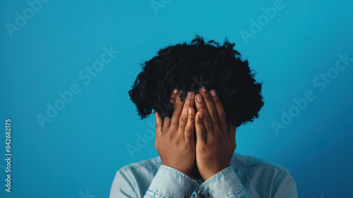 Person hiding face with hands on blue background