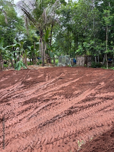 Photo of a freshly leveled land with clear JCB tyre marks, capturing the detailed impressions and textures in the soil, showcasing the raw and rugged aftermath of the leveling process.