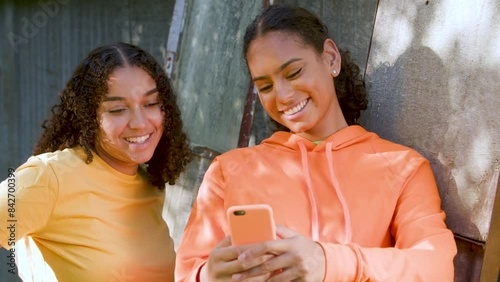 Two beautiful, happy, smiling mixed race African American girls teenagers young women outdoors in the city using a smartphone or cell phone for social media or text messaging. Slow motion 4K clip
