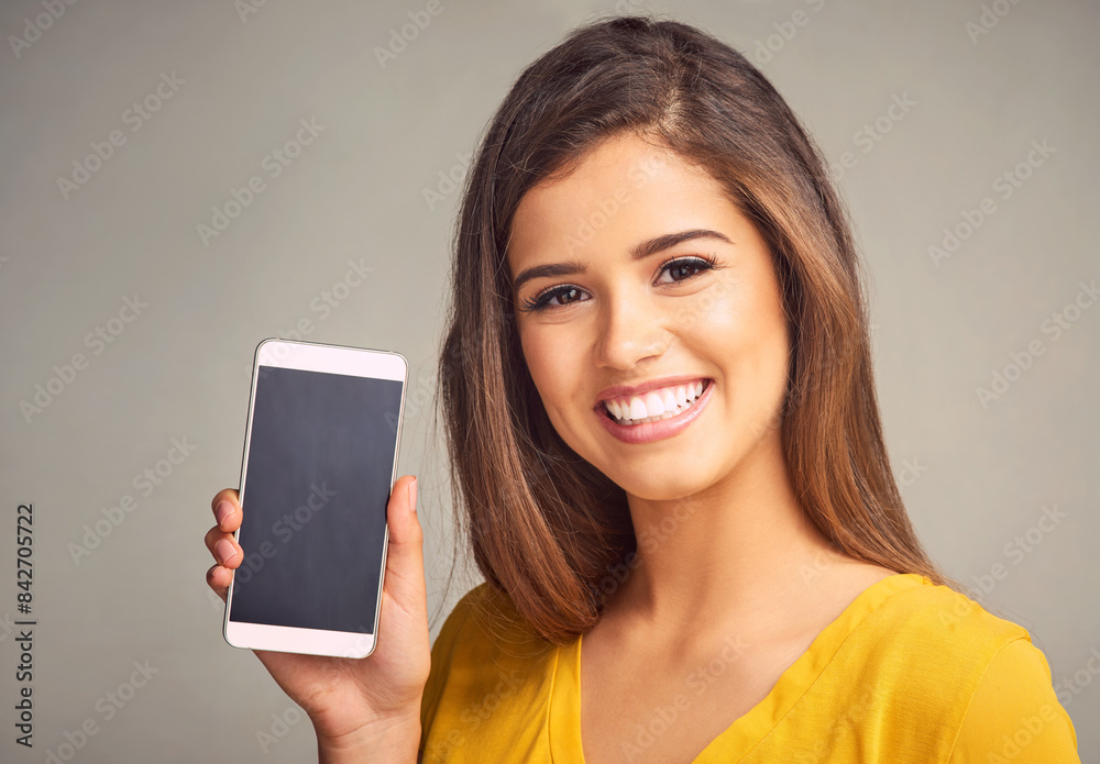 Happy, woman and display of phone in studio with mockup space for advertising, marketing or promotion. Portrait, technology and female person presenting cellphone screen isolated by gray background.