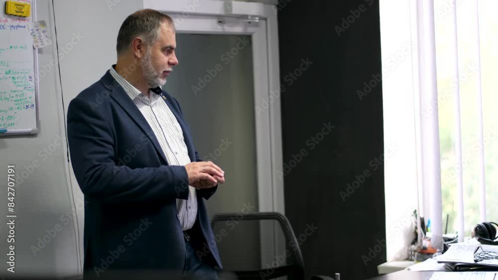 A man with a beard in a suit in the office waits and stands near the table. Adult male. office worker A man with a beard in a suit in the office waits and stands near the table. Adult male. office worker